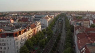 İleri, Schoenhauser Allee Bulvarı üzerinde yüksek tren yolu ve tren istasyonuyla uçar. Şehir merkezinin sabah hava görüntüsü. Berlin, Almanya
