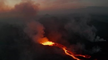 Aktif volkan patlamasının havadan görüntüsü. Erimiş lav kraterden aşağı akıyor, giden volkanik gazlardan oluşan bir kolon. Güneş doğmadan önce. Fagradalsfall volkanı. İzlanda, 2021