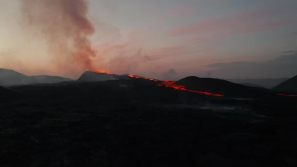 進む夜明けに火山の風景の上を飛ぶ。活火山から立ち上がる煙と地面に流れる溶岩流。ファグラダルフィオール火山。アイスランド、 2021年 — ストック動画