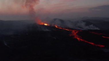 Şafak vakti aktif volkanın görüntüsü iniyor. Kaynayan magma kraterde sıçrıyor ve akıntılarda akıyor. Fagradalsfall volkanı. İzlanda, 2021