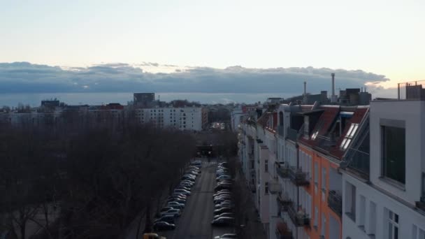 Vista aérea de los vehículos que se mueven en una dirección con coches estacionados en un lado de la calle rodeados de edificios tradicionales y árboles durante una mañana nublada en Berlín, Alemania — Vídeo de stock
