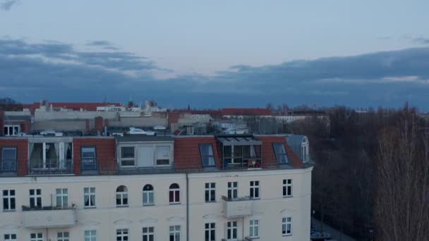 Vista aerea al rallentatore della tradizionale casa in mattoni sul tetto dall'altra parte della strada con veicoli parcheggiati e in movimento attraverso la corsia circondata da alberi su una nuvolosa mattina presto a Berlino, Germania — Video Stock