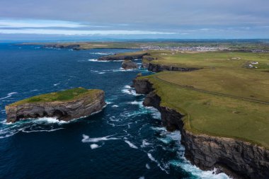 İrlanda 'nın ünlü turistik yeri Moher Cliff' in güzel ve yeşil dağının hava panoramik manzarası. Gün boyunca bulutlu gökyüzünün altında kayalara vuran deniz dalgaları.