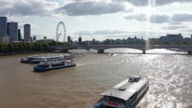 Thames Nehri 'nin ışıltılı su yüzeyinde yüzen gemiyi takip ediyoruz. Güneş ışığına karşı görüş. Londra 'nın Gözü ve Parlamento Binaları' nın silueti gökyüzündeki parlak bulutların üzerinde. Londra, İngiltere