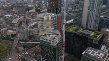 İnşaat sürecinde yüksek modern binanın yörüngesinde çekim yapıldı. İnşaat alanındaki kule vinci. Aşağıdaki caddelerin hava görüntüsü. Londra, İngiltere