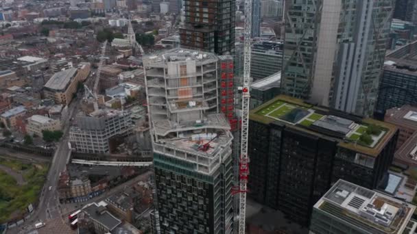 Orbit disparou em torno do edifício moderno alto no processo da construção. Guindaste torre no canteiro de obras. Vista aérea do tráfego nas ruas abaixo. Londres, Reino Unido — Vídeo de Stock