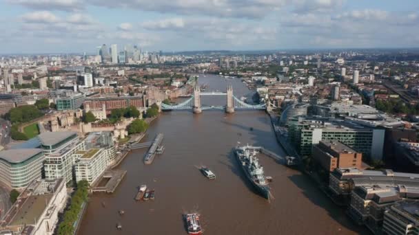 Widok z lotu ptaka na słynny Tower Bridge przez Tamizę. Statek muzeum HMS Belfast zacumował w ratuszu. Nowoczesne wieżowce w centrum finansowym Canary Wharf w tle. Londyn, Wielka Brytania — Wideo stockowe