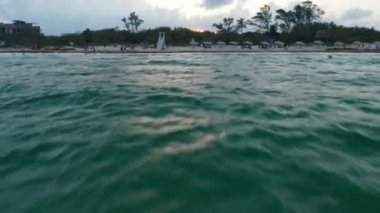 Drone su yüzeyinden kumlu sahile doğru uçuyor. Yükselen çekim, Meksika Playa del Carmen şehrini gözler önüne seriyor.