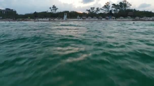Drone che vola sopra la superficie dell'acqua verso la spiaggia sabbiosa. Svolta crescente rivelando la città di Playa del Carmen, Messico — Video Stock