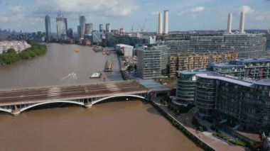 İleri, çok raylı demiryolu köprüsüne uçar. Nehir kıyısındaki modern apartmanlar. Arka planda uzun, modern gökdelenler. Londra, İngiltere
