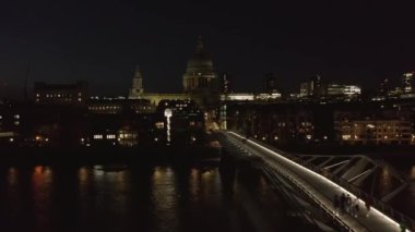 İnsanlar gece Millennium Köprüsü 'nde yürüyorlar. Mütevazı bir şekilde aydınlatılmış Aziz Paul Katedrali manzarası. Londra, İngiltere