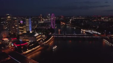 Gün batımından sonra şehrin havadan görüntüsü. Thames nehrinin üzerinde gece sineği, aydınlatılmış köprüler ve mor Londra gözü. Londra, İngiltere