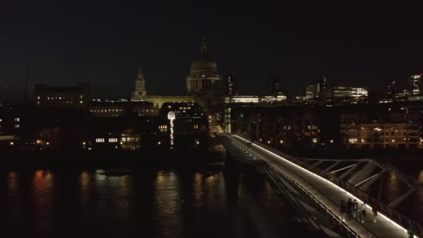 İnsanlar gece Millennium Köprüsü 'nde yürüyorlar. Mütevazı bir şekilde aydınlatılmış Aziz Paul Katedrali manzarası. Londra, İngiltere — Stok video