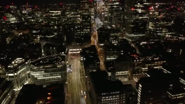 数階建ての建物の間の広いマルチレーン通りを走行する車両の後方を明らかにする。夜の街の空中ビュー。イギリスのロンドン — ストック動画