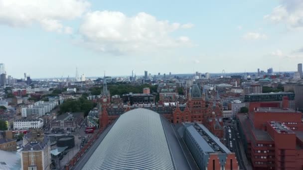Backwards fly above large building of St Pancras train station. Aerial view of roof over platforms in transport terminal. London, UK — Stock Video