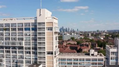 Beyaz yüzlü büyük bir binanın görüntüsü yükseliyor. Arka planda gökdelenler olan şehir manzarası ortaya çıkıyor. Londra, İngiltere