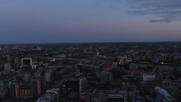 Forwards fly above urban borough after sunset. Heading towards illuminated Tower Bridge over River Thames. London, UK — Stock Video