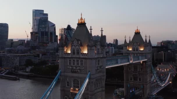 Поднятые кадры освещенной верхней аллеи и украшенных башен Тауэрского моста после заката. Небоскрёбы в районе Сити на заднем плане. Лондон, Великобритания — стоковое видео