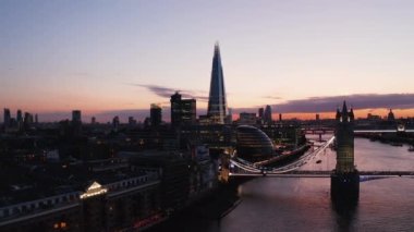 Thames Nehri üzerinde Tower Köprüsü 'nde akşam uçuşu. Toprak zemindeki binaların kaygan manzarası. Belediye binası ve Çömlek Parçası gün batımından sonra renkli gökyüzüne karşı. Londra, İngiltere