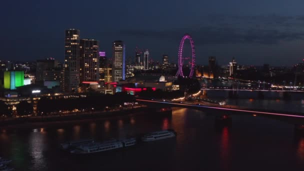 Voorwaarts vliegen boven de stad 's nachts. Verlichte gebouwen aan de waterkant van de Theems. Royal Festival Hall en violet licht op Londen oog. Londen, Verenigd Koninkrijk — Stockvideo