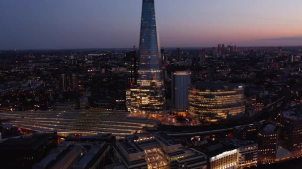 Slide and pan shot of illuminated London Bridge train station, News Building and Shard rascacielos. Vista aérea nocturna de la ciudad después del atardecer. Londres, Reino Unido — Vídeos de Stock