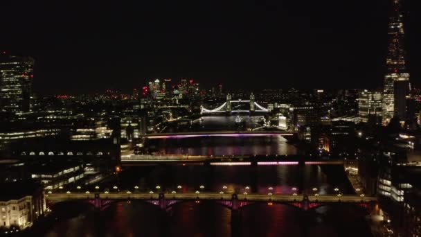 Ночной вид с воздуха на мосты через Темзу. Поезда и транспортные средства, проезжающие по мостам. Подсветка Тауэрского моста на заднем плане. Лондон, Великобритания — стоковое видео