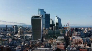 City 'nin finans merkezindeki modern gökdelenlerin kayma ve pan görüntüleri. Uzun ofis binaları öğleden sonra güneş ışığıyla aydınlanıyor. Londra, İngiltere