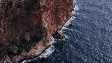 İspanya 'nın engebeli Mallorca kıyısındaki görkemli kızıl kayalıklara çarpan yoğun mavi deniz manzarası..