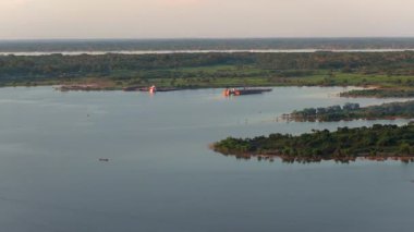 Amazon Nehri 'nde, yemyeşil yağmur ormanlarıyla çevrili sanayi gemileri ve küçük teknelerin hava görüntüleri..