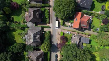 Almanya, Hamburg 'da sakin bir banliyö caddesinin üzerinde uçan tepeden aşağıya doğru perspektif. Yeşil bahçeler, arabalı evler ve beyaz bir kamyon.