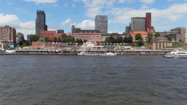 Hamburg kıyısı boyunca yan yana uçan hava manzarası Landungsbruecken rıhtımını, modern binaları ve Elbe Nehri 'ndeki tekneleri gösteriyor.