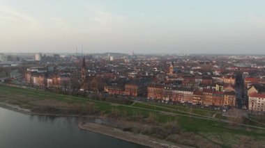 Almanya 'nın Mannheim kentinin geniş hava manzarası, gün batımında tarihi binalarla birlikte Neckar nehrinin yanında uçuyor..