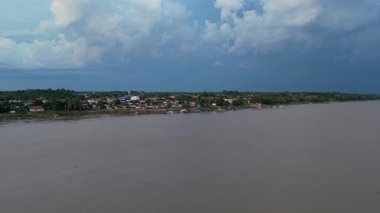 Amazon Nehri 'nin geniş, çamurlu sularında, uzak kıyılarda yemyeşil yağmur ormanlarıyla yol alan büyük bir yolcu teknesinin havadan görüntüsü..