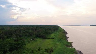 Uçsuz bucaksız Amazon nehrinin sınırındaki küçük bir köy dramatik bulutlu bir gökyüzünün altında. Yoğun ormanı ve mütevazı evleri vurgulayan hava görüntüleri.