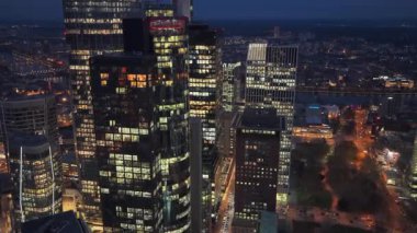 Frankfurt am Main 'in finans bölgesindeki aydınlık ofis binalarının yörüngesinde gece çekimleri. Karanlıkta parlayan modern gökdelen mimarisi.