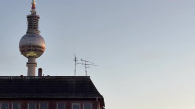 Berlin 'de Alexanderplatz' ın üzerinde duran ikonik Fernsehturm televizyon kulesi. El kamerası görüntüsü antenli tipik bir binanın çatısını yakalıyor.