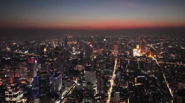 Gün batımında parlayan Bangkoks siluetinin havadan görüntüsü. Şehir ışıkları sokakları aydınlatıyor ve şehir merkezinde modern gökdelenler var..