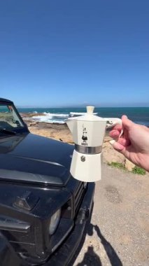 İspanya 'nın Cadiz kentindeki La Caleta Sahili' nin pitoresk bir manzarası. Atlantik Okyanusu 'nun arka planında siyah bir SUV ve Bialetti moka demliği var..