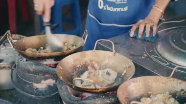 Sokak satıcısı kömür ocağının üstünde tavada yumurtayla geleneksel erişte pişiriyor. Otantik Bangkok aşçılık sahnesini kapat.