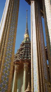 Bangkok, Tayland 'daki Grand Palace kompleksi içinde açık mavi gökyüzüne karşı Wat Phra Kaew' daki altın çadırı alçak açılı dikey görüntüsünü kapatın..