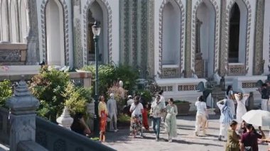 Çeşitli turist kalabalığı Bangkok, Tayland 'daki tarihi bir tapınağın güneşli avlusunda geziyor. Süslü mimariye hayran kalıyorlar..