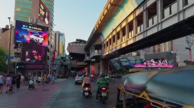 BTS Skytrain İstasyonu 'nun altındaki hareketli bir Bangkok sokağı renkli reklam panoları ve yoğun trafiğiyle Siyam Meydanı' nın canlı enerjisini yakalıyor..