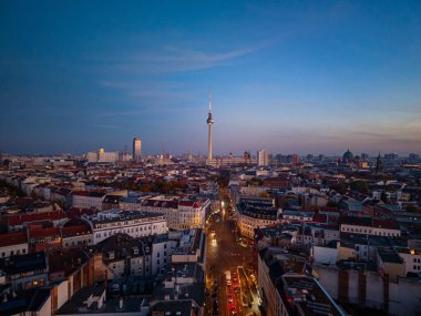 Berlin TV kulesi, çarpıcı bir dönüm noktası, alacakaranlıkta şehir manzarası üzerinde beliriyor, kentsel ufuk çizgisini havadan gelen sıcak bir ışıkla aydınlatıyor..