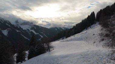 Kış tatilinde Alpler 'deki karlı dağ vadisine tepeden bakan tepede köknar ağaçları ve yamaçlı kayak merkezleri var..