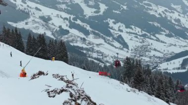 Kayakçılar, bir kış günü Avusturya 'da eşsiz bir tripod hava perspektifinden arka planda hareket eden bir gondolla Alplerdeki karlı dağ yamacından inerler..