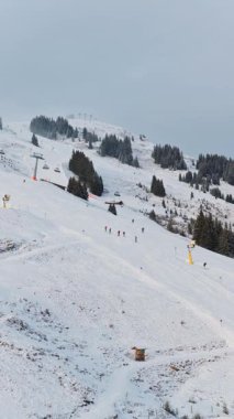 Avusturya 'nın Saalbach kentindeki soğuk bir sabahta Alpler' deki bir kış otelinde karlı bir yamaçtan inen kayakçıların dikey videosu..