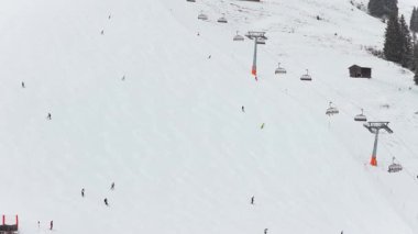 Avrupa Alpleri 'nde kış tatili sırasında bir teleferiğin yanındaki karlı dağ yamacından inen kayakçıların üç ayaklı hava perspektifi.