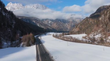 Güneşli bir kış günü, Saalbach 'taki karlı Avusturya Alpleri vadisinde asfalt yolda giden arabaların durağan hava manzarası mavi gökyüzü ve dağlarla.
