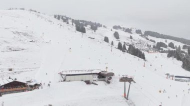 Avusturya 'nın Saalbach şehrinde bir kış günü Alplerde kayakçılar, bir teleferik istasyonu ve bir dağ kulübesi görülüyor..