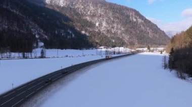 Avusturya Alplerinde kışın Saalbach yakınlarında kar ve dağlarla çevrili bir yolda araba ve kamyonların yüksek açılı perspektifi.